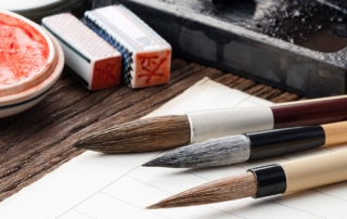 A closeup of exquisite Chinese calligraphy brushes, paper, ink, and stamps on an antique wooden desktop.